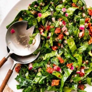 A serving bowl containing raw collard greens salad with salad servers.