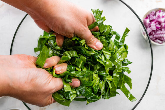 Hands massaging oil into chopped collard greens.