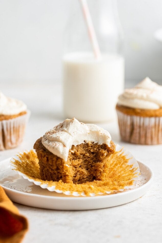 An unwrapped sweet potato cupcake with a bite taken out of it resting on a plate.