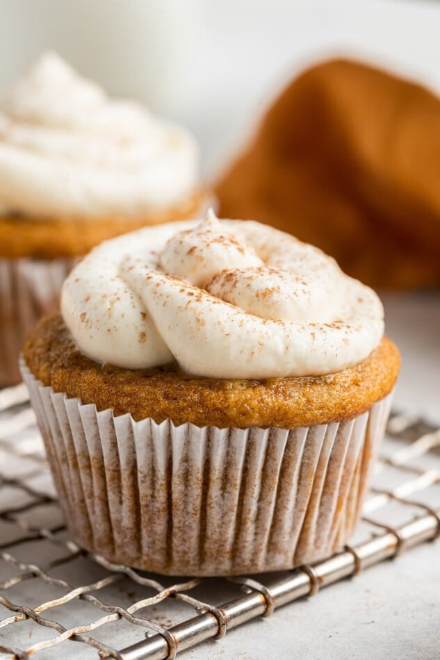 A frosted sweet potato cupcake wrapped in a paper liner resting on a wire cooling rack.