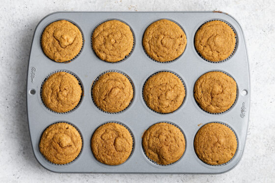 Twelve baked sweet potato cupcakes in a muffin tin.