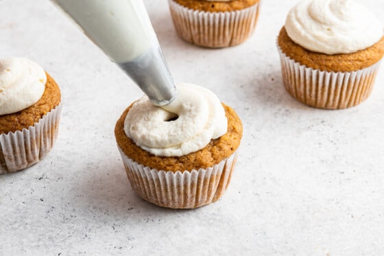 Frosting a sweet potato cupcake with an icing bag.