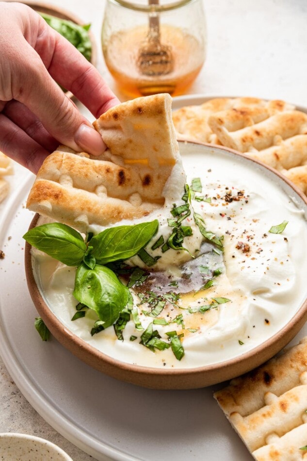 A hand scooping a piece of pita into dip.