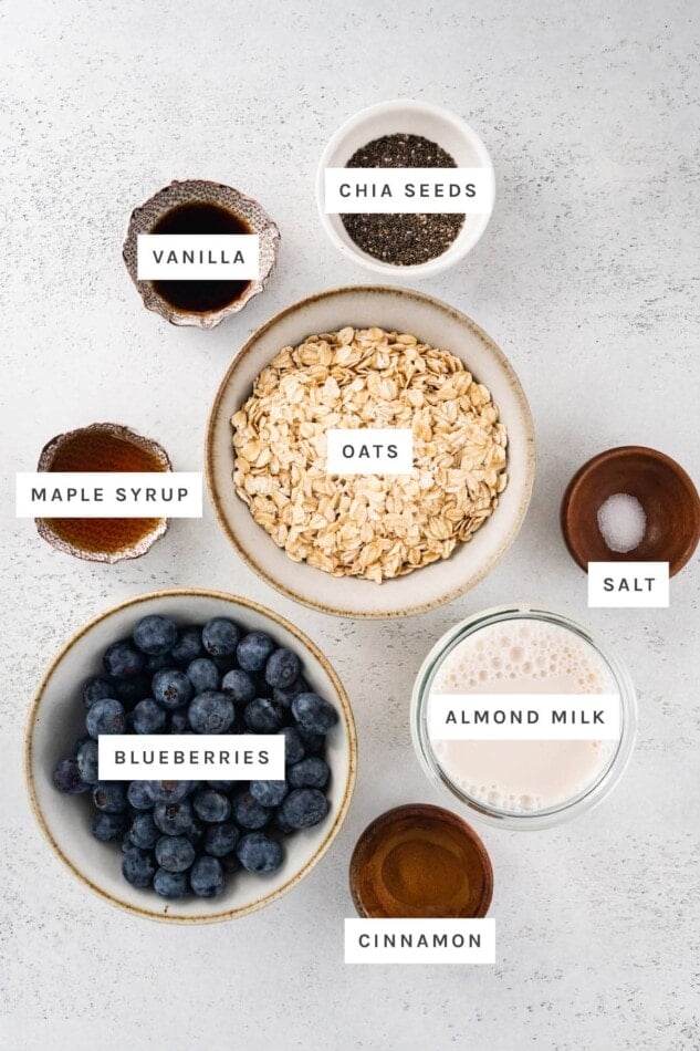 Ingredients measured out to make Blueberry Oatmeal: vanilla, chia seeds, maple syrup, oats, salt, blueberries, almond milk and cinnamon.