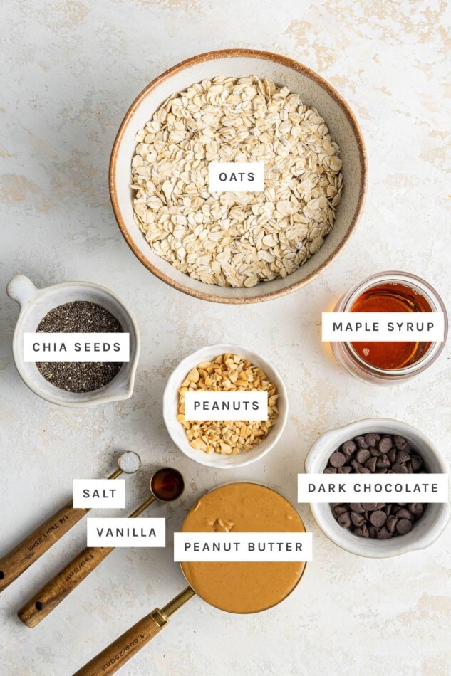 Ingredients measured out to make Chocolate Peanut Butter Granola Bars: oats, chia seeds, maple syrup, peanuts, dark chocolate, salt, vanilla and peanut butter.