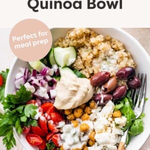 A Mediterranean Quinoa Bowl with quinoa, arugula, chickpeas, tomatoes, red onion, cucumbers, kalamata olives, feta cheese and hummus drizzled with tzatziki.