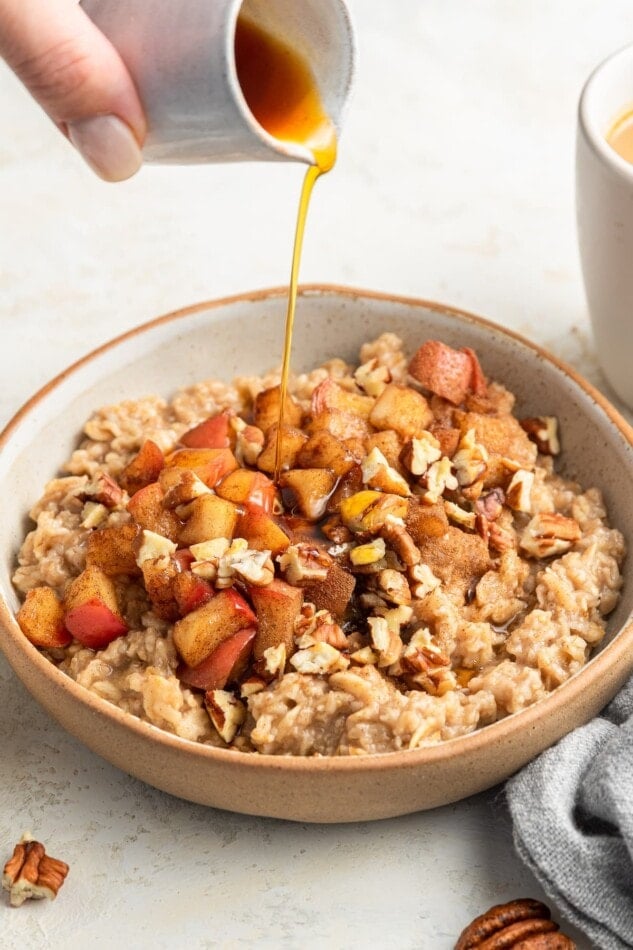 Maple syrup drizzled overtop a bowl of apple cinnamon oatmeal.
