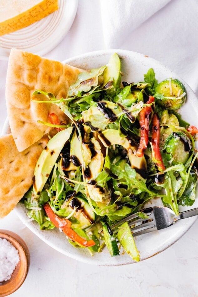 A bowl of salad drizzled with dressing and served with pita wedges.