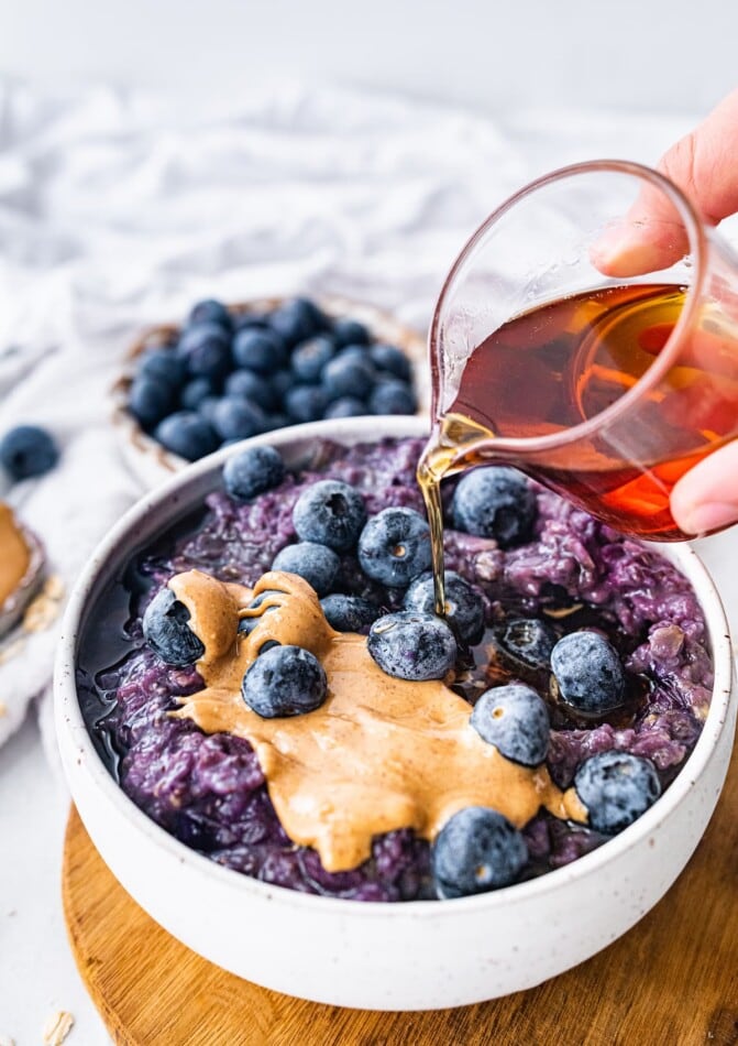Drizzling maple syrup on top of a bowl of blueberry oatmeal.