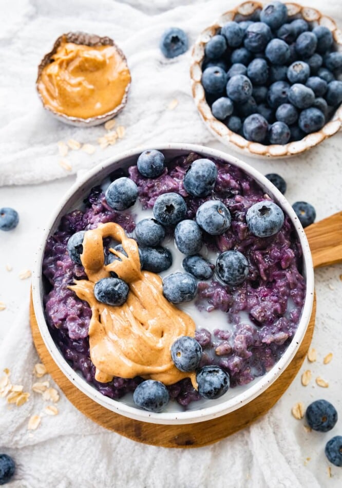 A bowl of blueberry oatmeal topped with blueberries, peanut butter and extra almond milk.