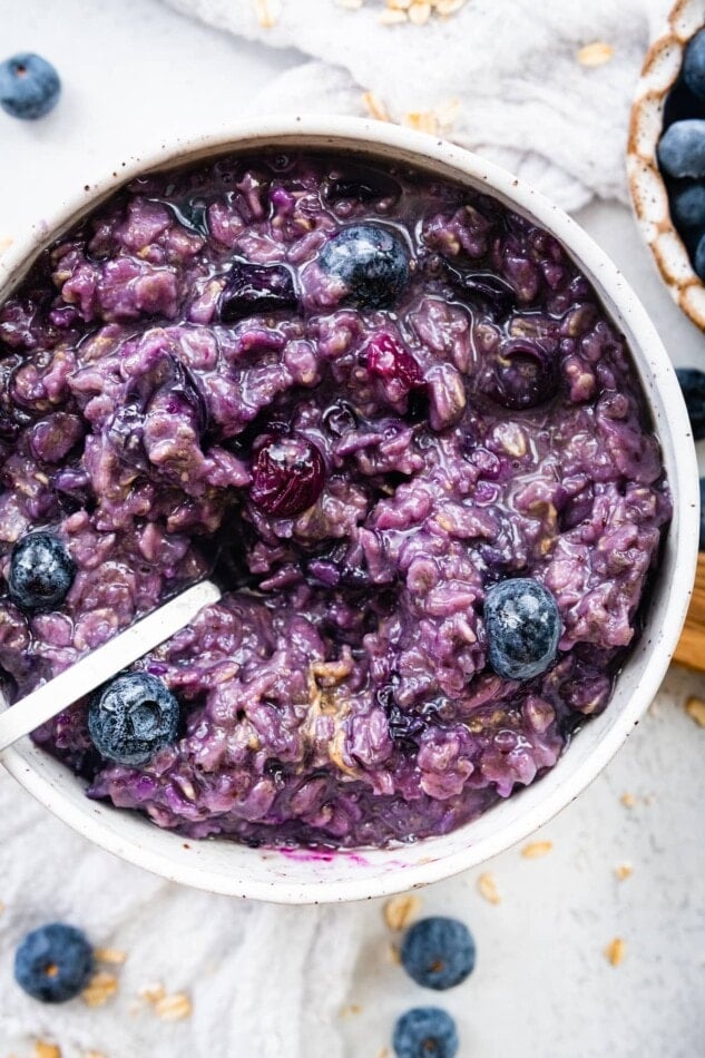A bowl of blueberry oatmeal with a spoon.