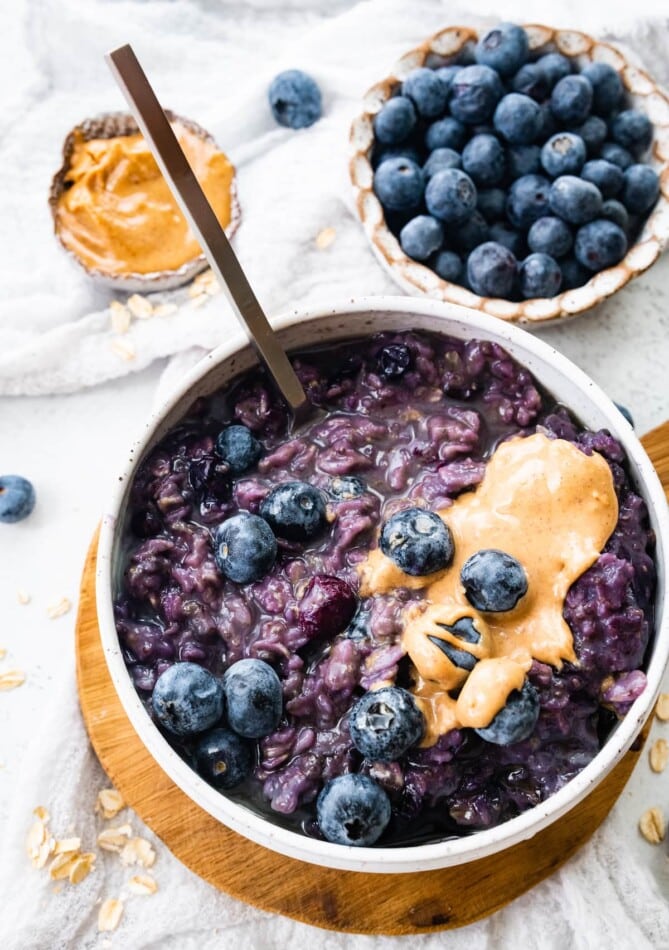 A bowl of blueberry oatmeal topped with blueberries and peanut butter with a spoon.
