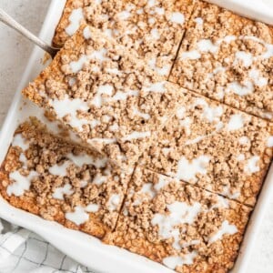 Portioned squares of coffee cake baked oatmeal in a baking dish, a square serving is being removed.