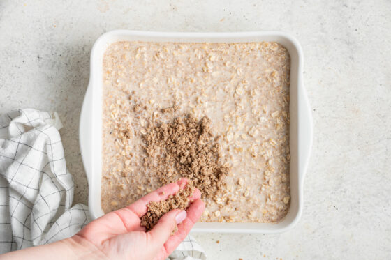 Sprinkling topping onto square baking dish containing oatmeal ingredients.