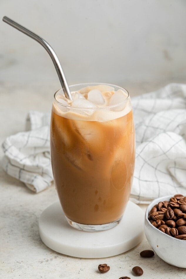 Protein coffee in a glass served over ice with a straw.