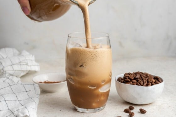 Pouring protein coffee over ice into a glass.