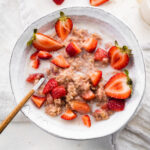 A bowl of strawberries and cream oatmeal with a spoon.