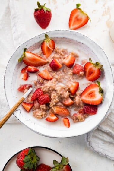 A bowl of strawberries and cream oatmeal with a spoon.