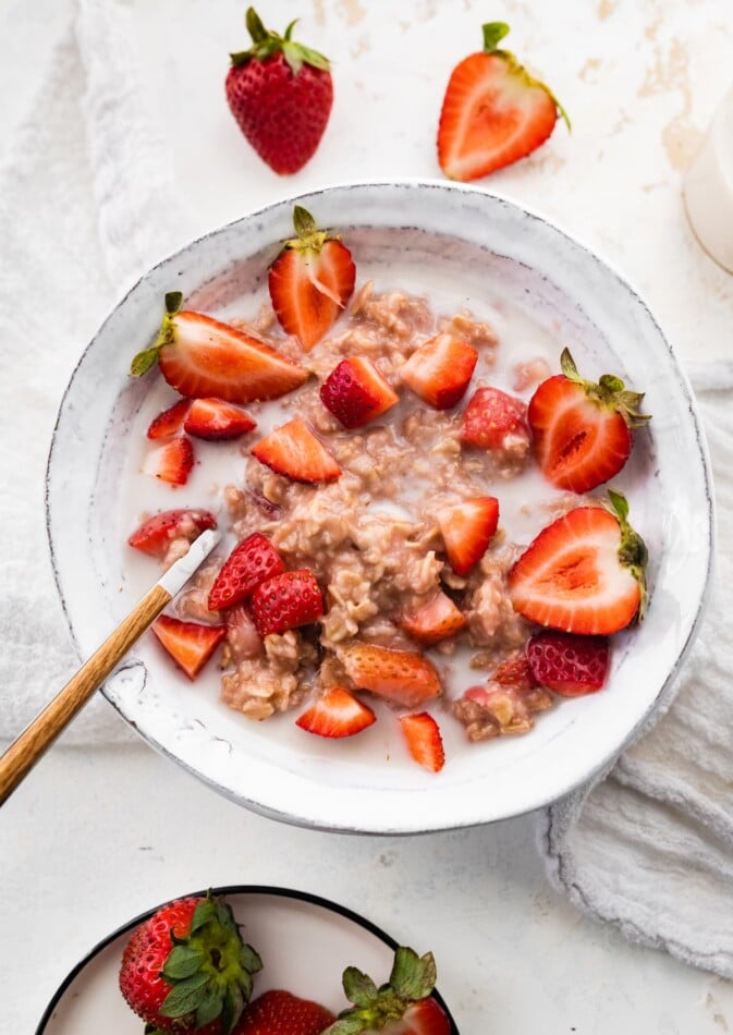 A bowl of strawberries and cream oatmeal with a spoon.