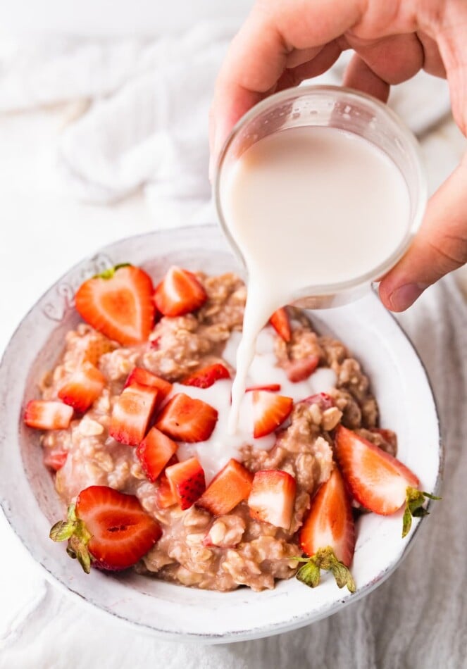 Pouring milk over a bowl of strawberries and cream oatmeal.