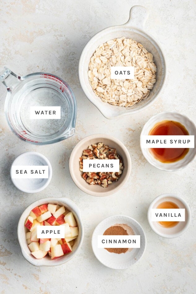 Ingredients measured out to make Apple Cinnamon Oatmeal: oats, water, maple syrup, apple, cinnamon, vanilla, sea salt and pecans.