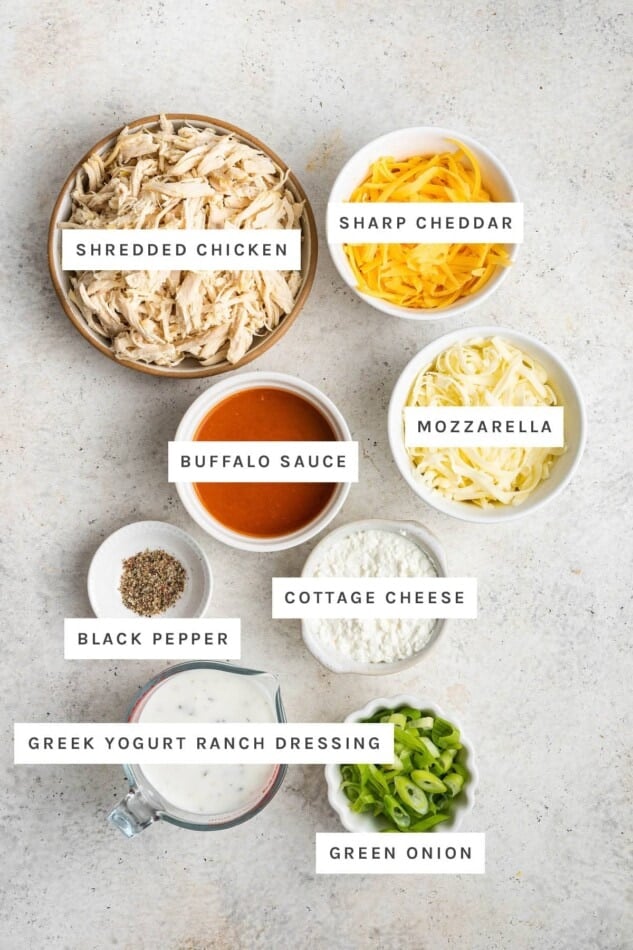 Ingredients measured out to make Healthy Buffalo Chicken Dip: shredded chicken, cheddar, buffalo sauce, mozzarella, black pepper, cottage cheese, Greek yogurt ranch dressing and green onion.