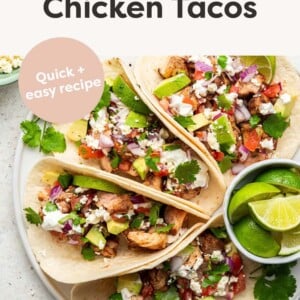 Four chicken tacos topped with cheese, avocado, cilantro and onion.