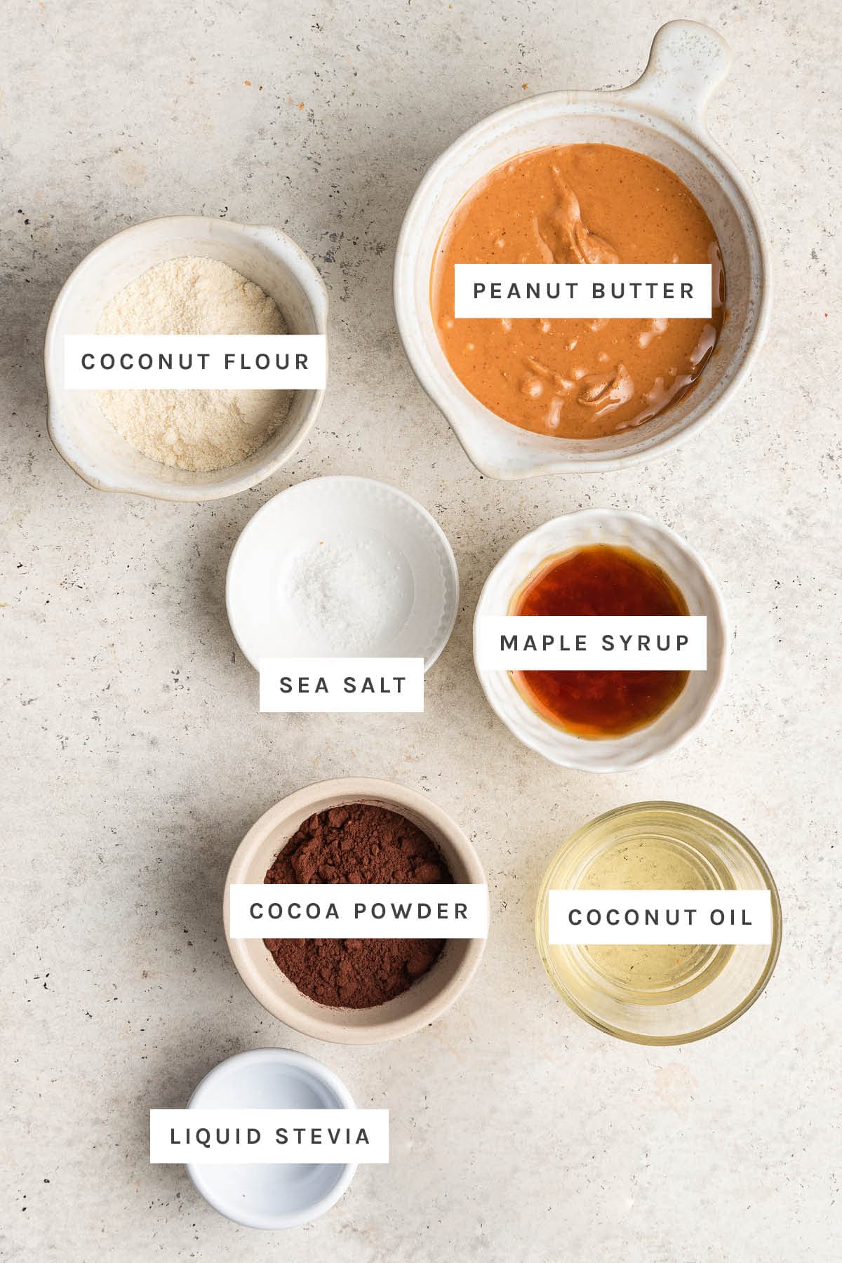 Ingredients measured out to make Healthy Peanut Butter Eggs: coconut flour, peanut butter, sea salt, maple syrup, cocoa powder, coconut oil and liquid stevia.