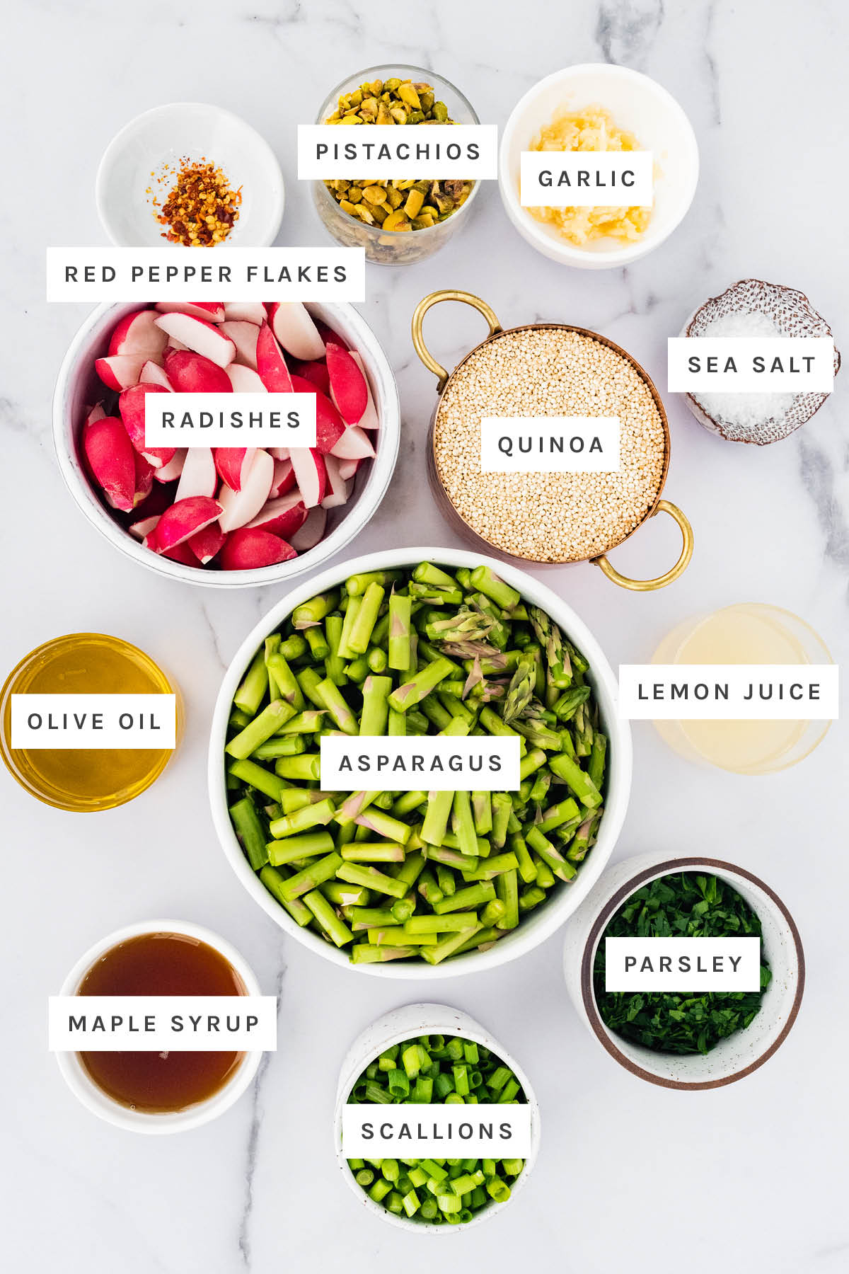Ingredients measured out to make Spring Quinoa Salad: red pepper flakes, pistachios, garlic, radishes, quinoa, sea salt, olive oil, asparagus, lemon juice, maple syrup, scallions and parsley.