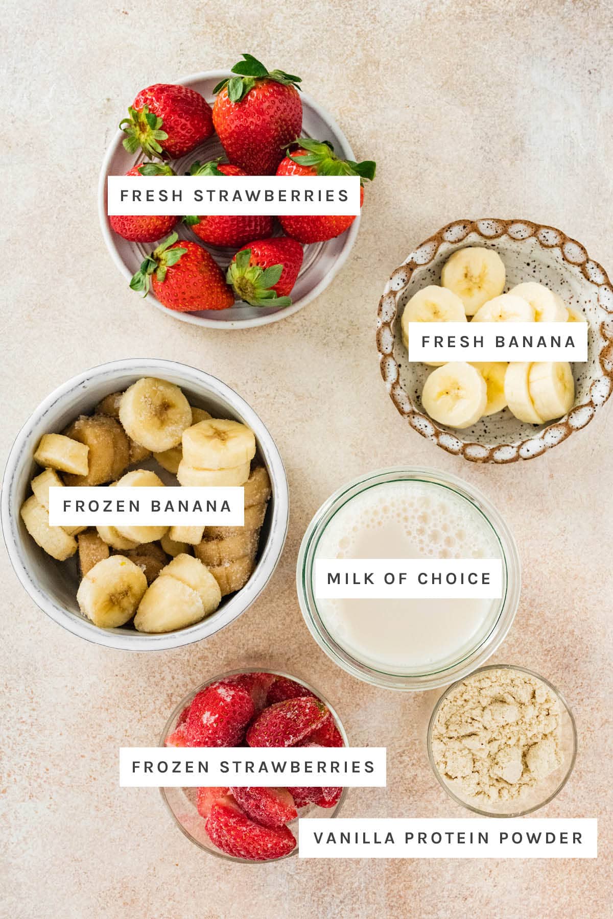 Ingredients measured out to make a Strawberry Banana Protein Smoothie: fresh and frozen strawberries, fresh and frozen banana, milk and vanilla protein powder.