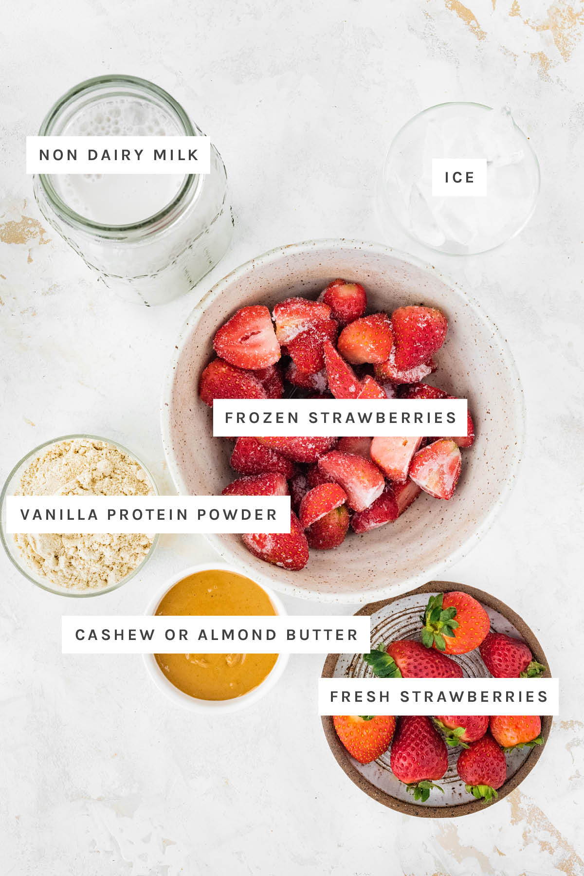 Ingredients measured out to make a Strawberry Protein Shake: non dairy milk, ice, frozen strawberries, vanilla protein powder, cashew or almond butter, fresh strawberries.