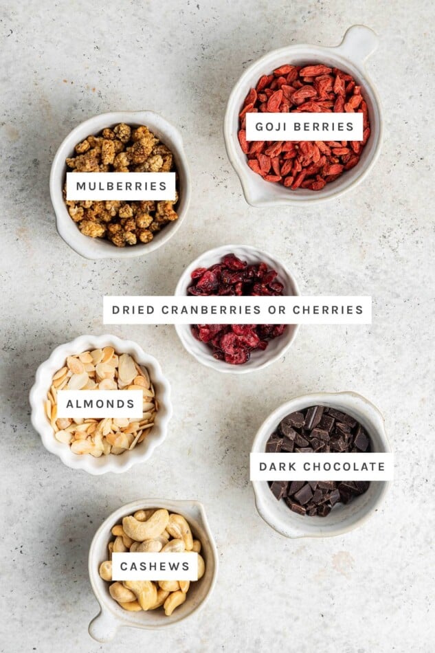 Ingredients measured out to make Superfood Trail Mix: goji berries, mulberries, dried cranberries, almonds, dark chocolate and cashews.