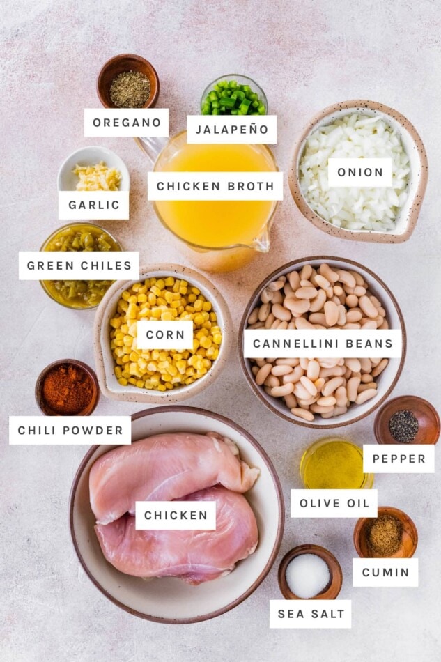 Ingredients measured out to make Healthy White Bean Chicken Chili: oregano, jalapeño, onion, broth, garlic green chiles, corn, cannellini beans, chili powder, chicken, olive oil, pepper, cumin and salt.