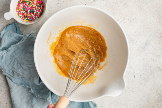 Egg, maple syrup, cashew butter, coconut oil, almond extract, vanilla extract and butter extract being whisked together in a bowl.