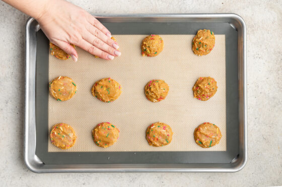 Balls of dough being pressed down with a hand.