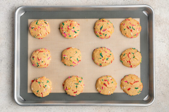 Twelve baked birthday cake cookies.