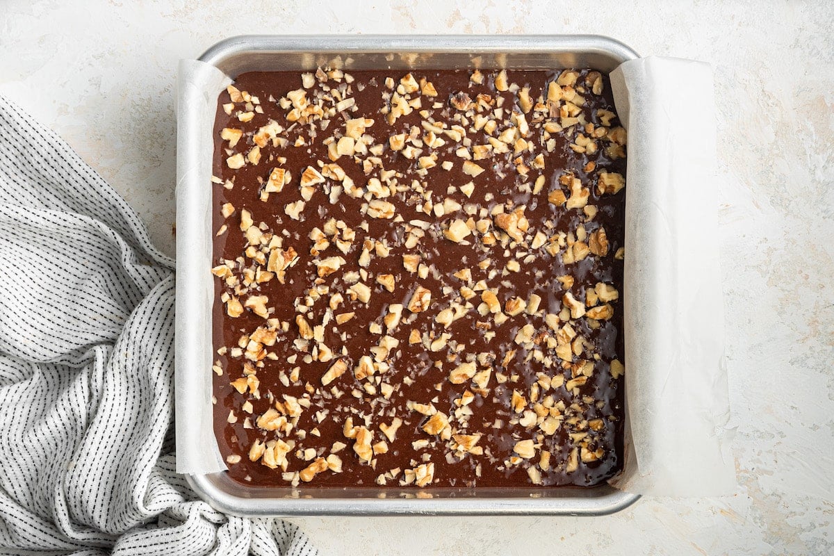 Brownie batter in a square baking pan topped with chopped walnuts.