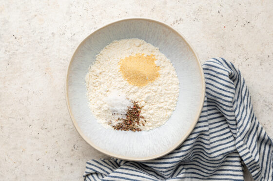 A bowl of flour, salt, pepper and garlic powder.