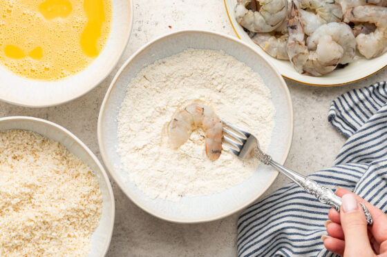 A fork dipping a shrimp into the flour mixture.