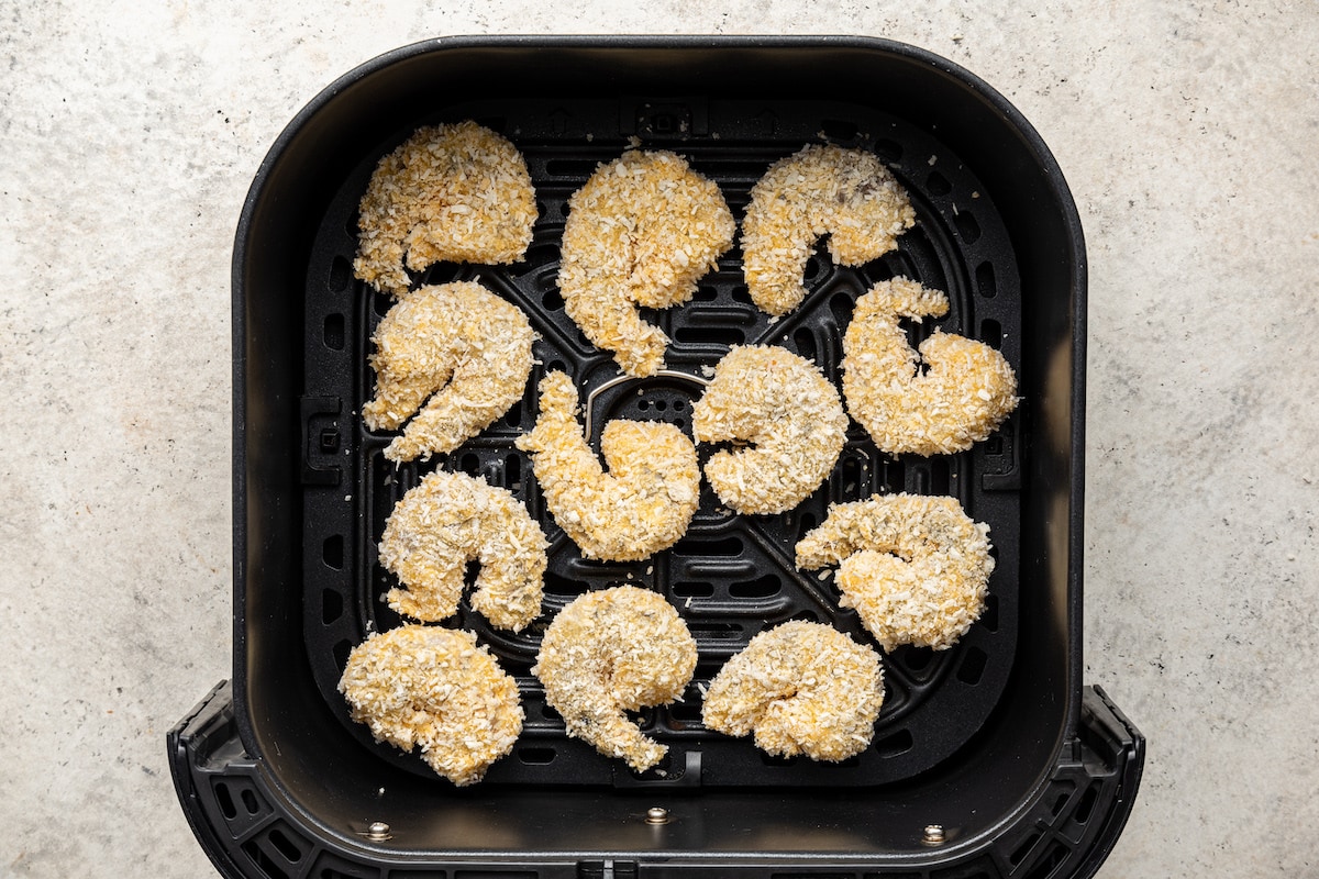 Coated shrimp arranged in the bucket of an air fryer.