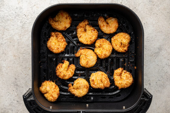 Coconut shrimp in the bucket of an air fryer.