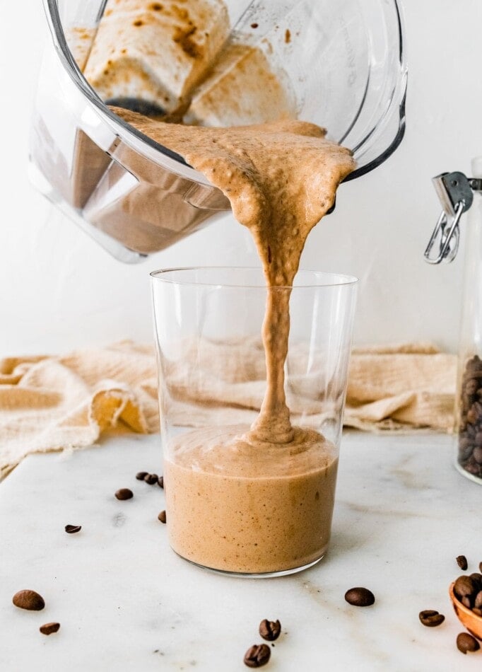 Pouring coffee protein shake into a glass from a blender.