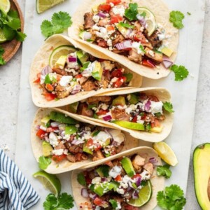 Chicken tacos in a row on a serving board.