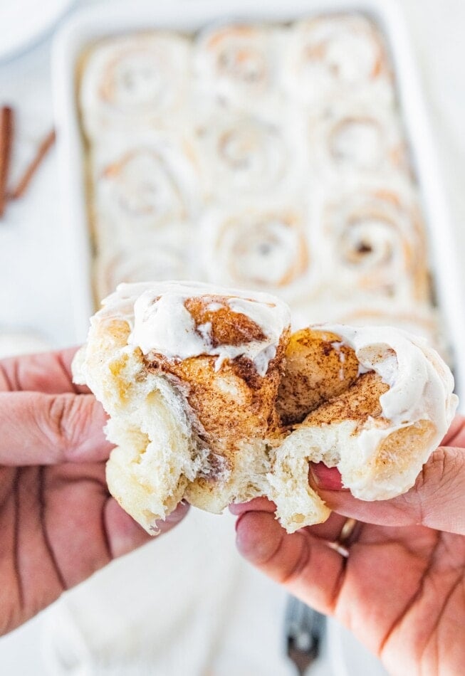 Two hands pulling apart a cinnamon roll.