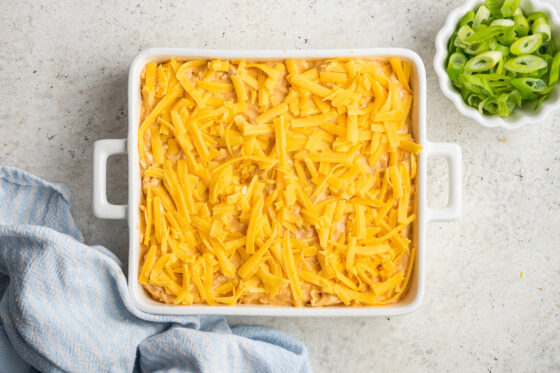 Buffalo chicken dip mixture in a baking dish topped with cheddar cheese.