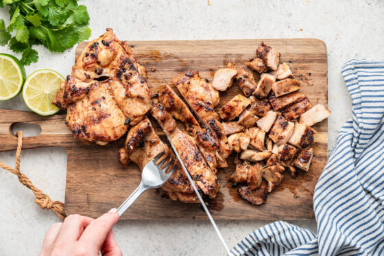 Slicing grilled chicken on a cutting board.