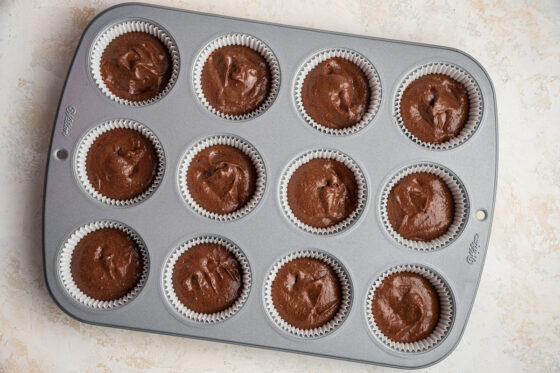 Batter portioned into twelve lined cupcake cavities.