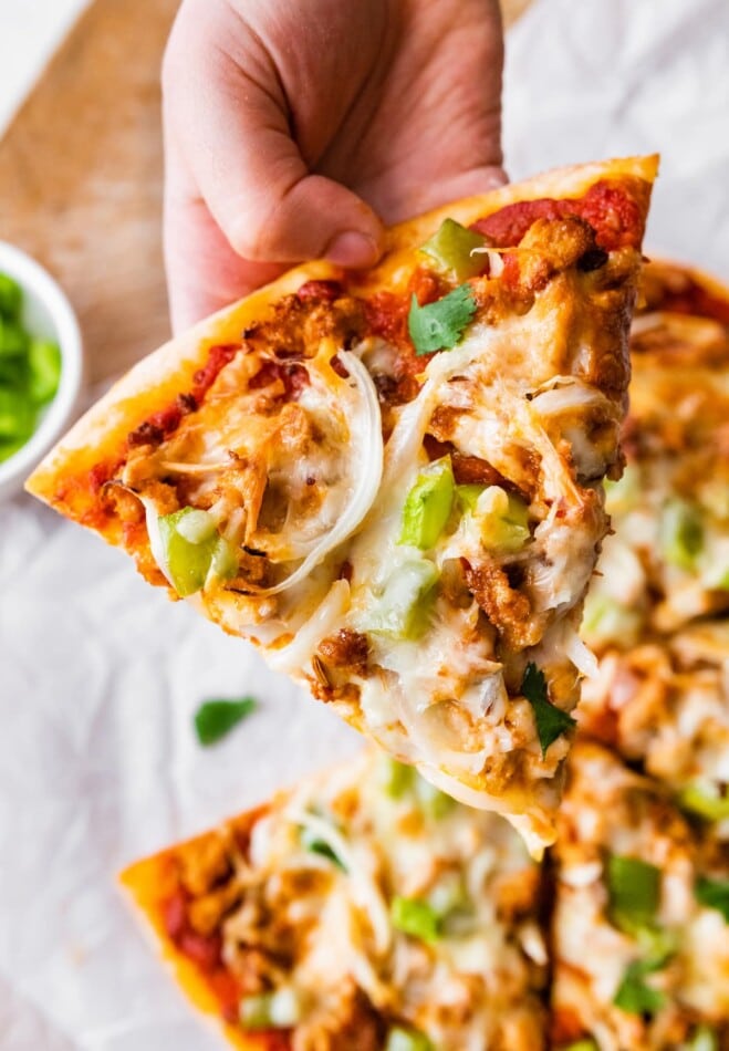 A hand holding up a slice of pizza.