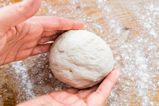 A ball of pizza dough between two hands.