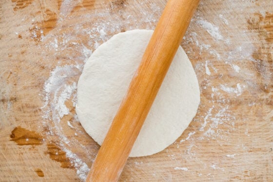 A rolling pin rolling out a circle of pizza dough.